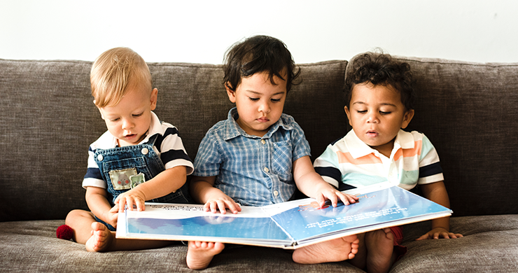 Three young toddlers sitting on a couch with a picture book